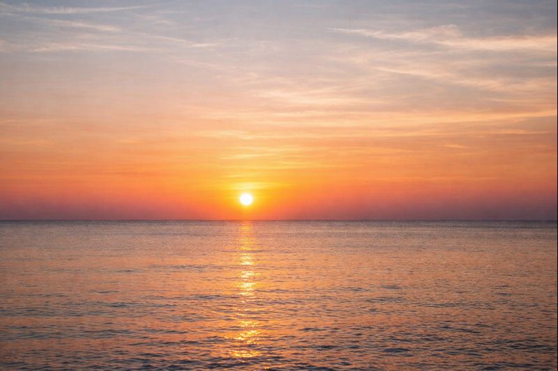 Sonnenuntergang über dem ruhigen Meer mit orangefarbenem Himmel und sanften Wellen.